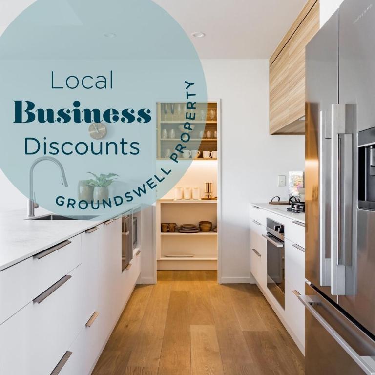 a kitchen with white cabinets and a refrigerator at Wainui Townhouses, Two Modern, Waterfront Units in Raglan