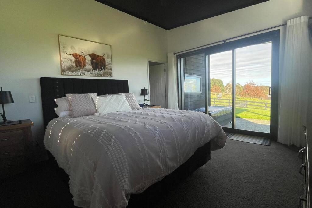 a bedroom with a bed and a large window at Ramarama retreat, farm views, spa bath & deer in Ramarama
