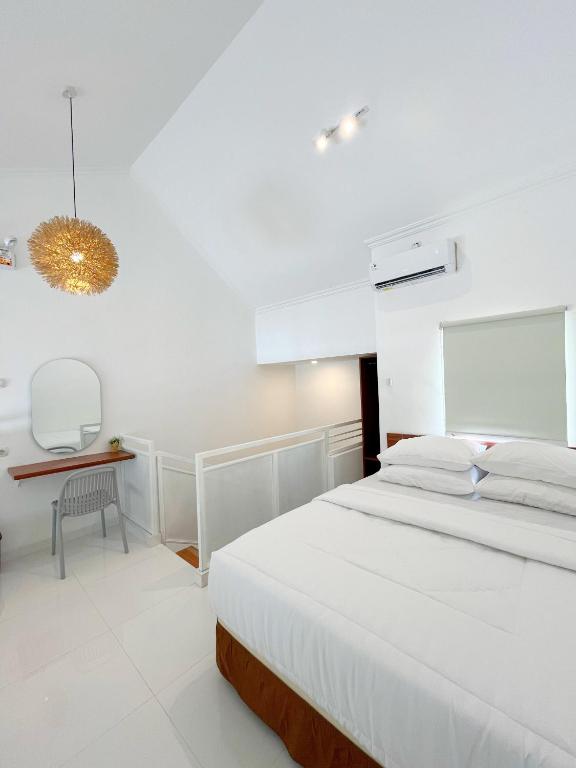 a white bedroom with a bed and a desk at Sampai Living Tugu in Yogyakarta
