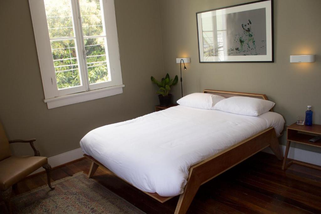 um quarto com uma cama com lençóis brancos e 2 janelas em El Navegante B&B em Valparaíso