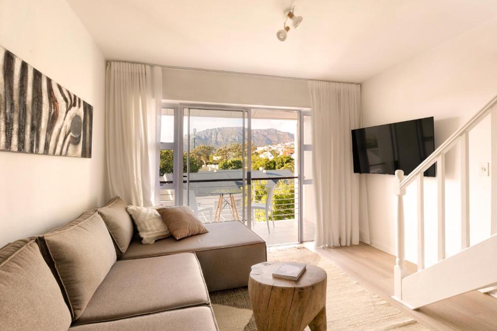 a living room with a couch and a large window at Four Peaks Duplex - 4 Sleeper with Mountain Views, Balcony and Pool in Hout Bay Beachfront in Hout Bay