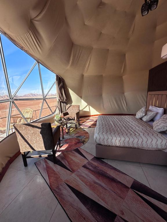 a bed and a chair in a room with a large window at Camille WadiRum Camp in Disah