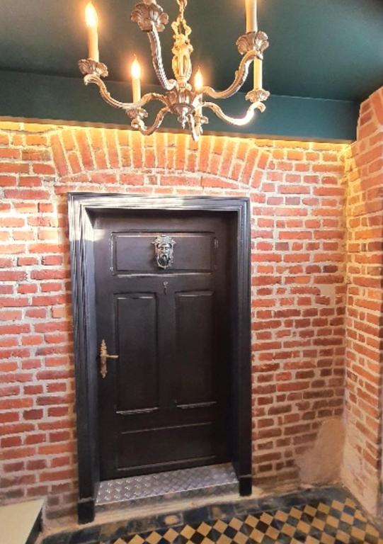 a black door in a brick wall with a chandelier at Apartament wiejska chata 150m2 in Piece