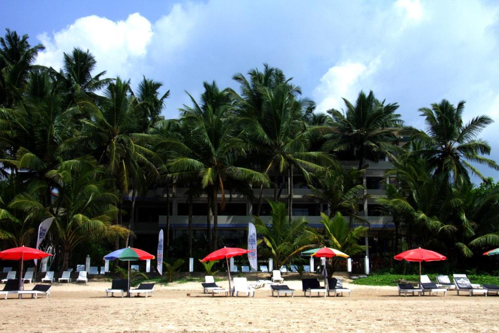 a beach with chairs and umbrellas and palm trees at Jagabay Resort & Surfing School in Weligama