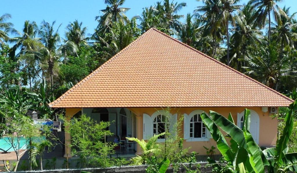 a house with an orange roof and some palm trees at Villa Mimosa in Lovina
