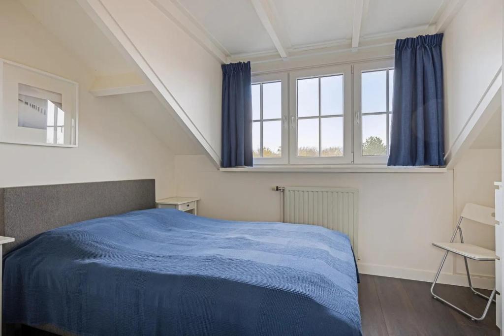 Un dormitorio con una cama azul y dos ventanas. en Duinstraat 10, en Domburg