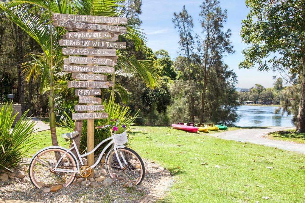 Una bicicleta estacionada al lado de un cartel con letreros. en Seven Mile Beach Holiday Park, en Gerroa