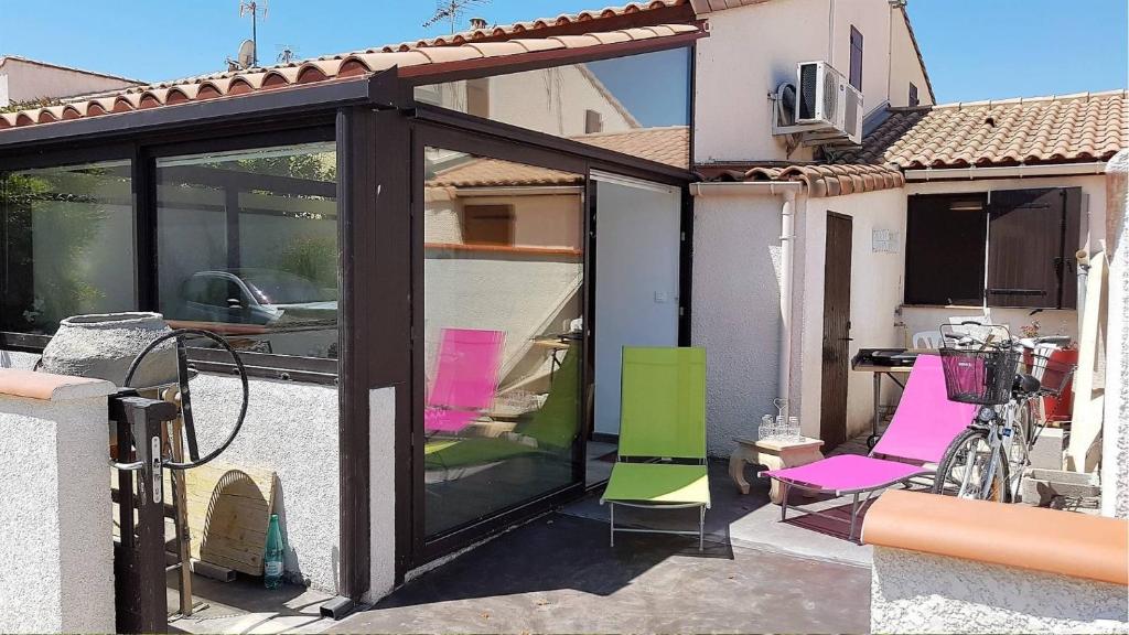 une extension d'une maison avec des chaises roses et vertes dans l'établissement Superbe pavillon de vacances climatisé avec piscine collective -6CYC62, à Saint Cyprien Plage