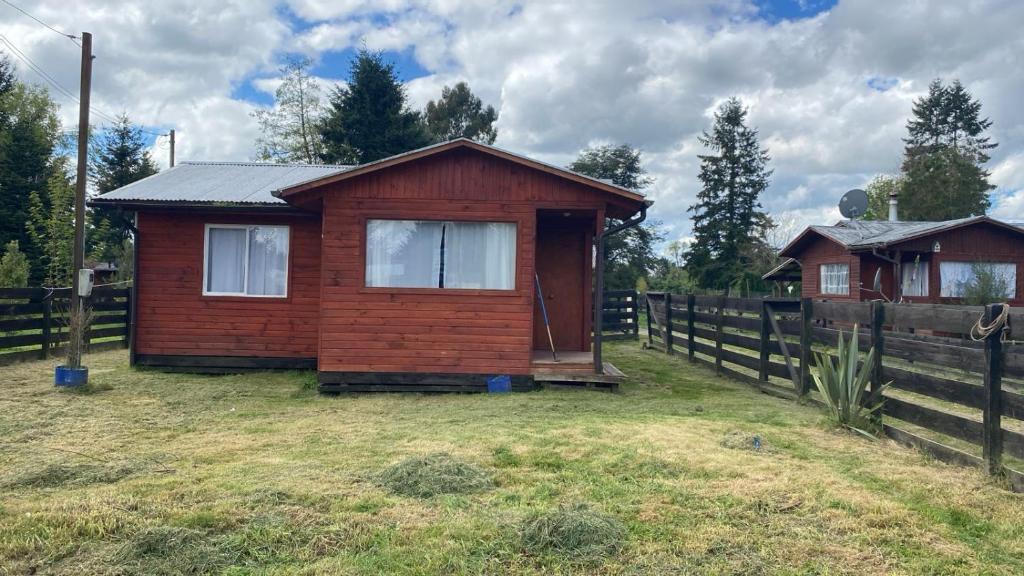 a small wooden house in a field next to a fence at Cabañas Doña Norma in Puyehue