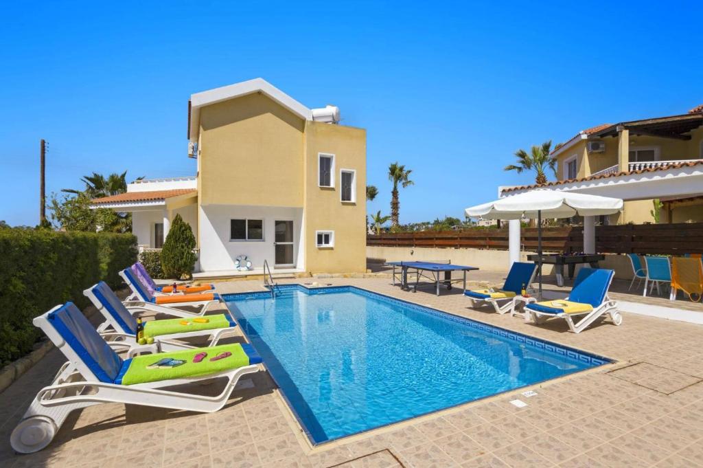 a swimming pool with chairs and a table and a house at Villa Azalea by Villa Plus in Peyia