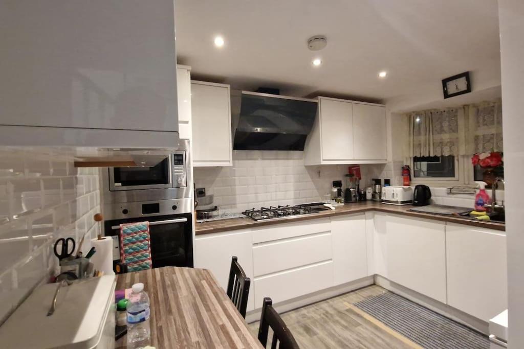a kitchen with white cabinets and a wooden table at Lizola Homes Rooms in Dagenham