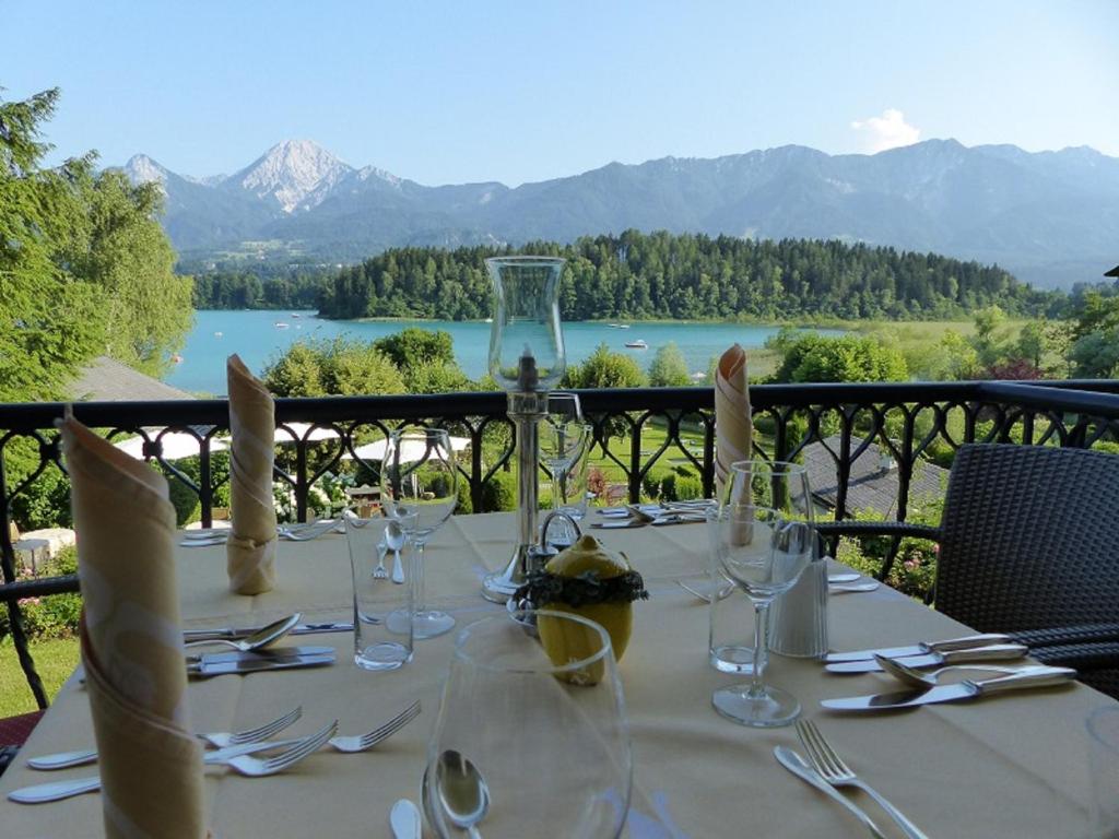 a table with glasses and utensils and a view of a lake at Seehotel Ressmann in Drobollach am Faaker See