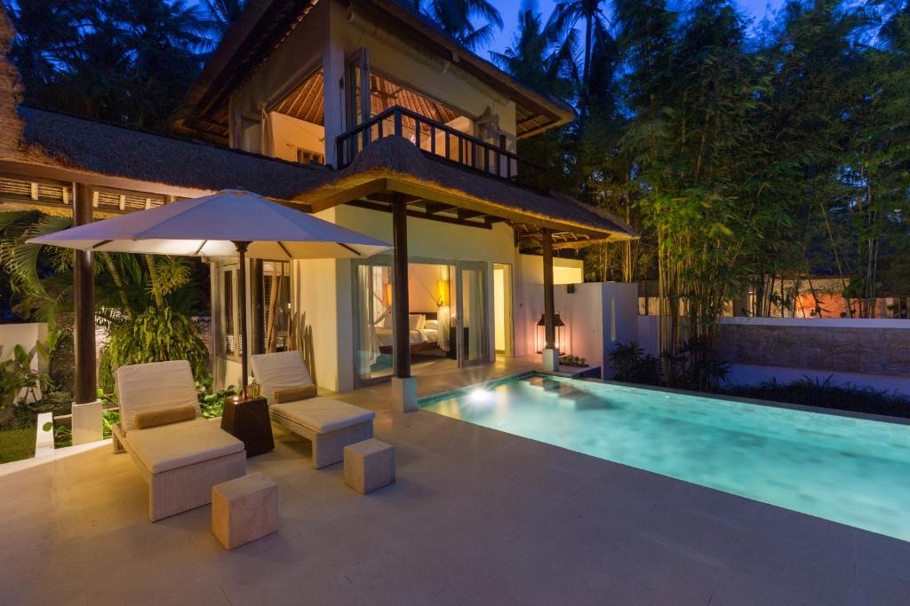 a house with a swimming pool and two chairs and an umbrella at New Moon in Ubud