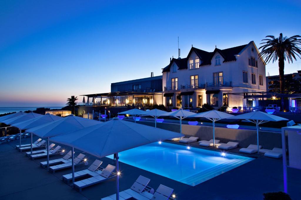 a hotel with a pool and umbrellas and a building at Farol Hotel in Cascais
