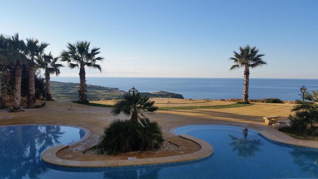 una piscina con palmeras y el océano en el fondo en CSB Apartment, en Żebbuġ