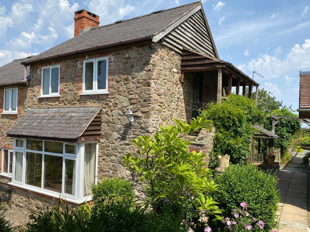 a stone house with white windows and bushes at Curlew Cottage in Shrewsbury