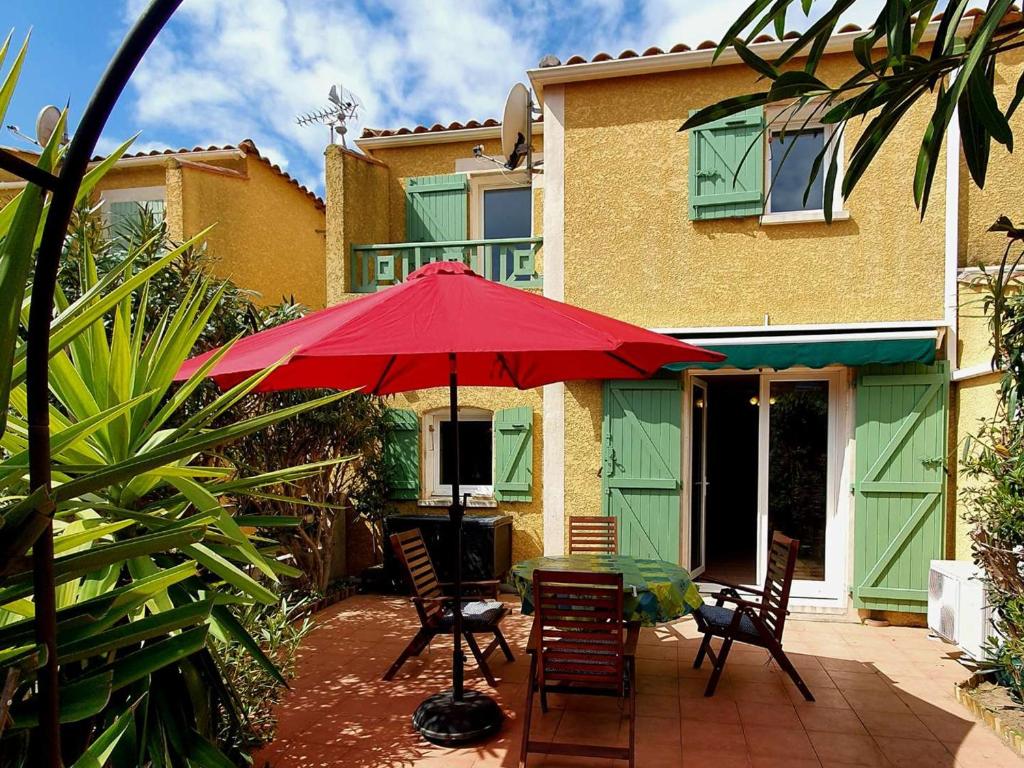 un patio avec une table, des chaises et un parasol rouge dans l'établissement Charmante Villa Climatisée à Narbonne-Plage, Proche Mer, 6 Personnes, 3 Chambres, Parking Privé - FR-1-409-120, à Narbonne-Plage