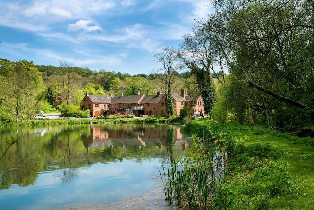 a house next to a pond in front of a house at Travel Fox Cottages- Swimming Lake, BBQ Hut, Games Area - Alton Towers in Froghall