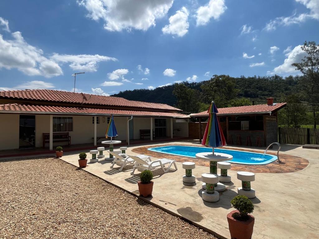 a pool with chairs and umbrellas in front of a house at Chácara Barone - Chácara em SerraNegra in Serra Negra