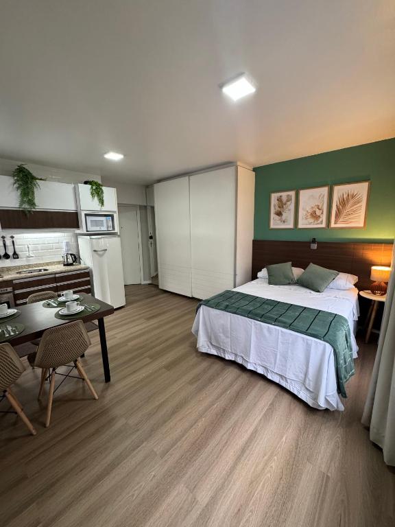 a bedroom with a bed and a table and a kitchen at Loft Studio no Kobrasol in São José