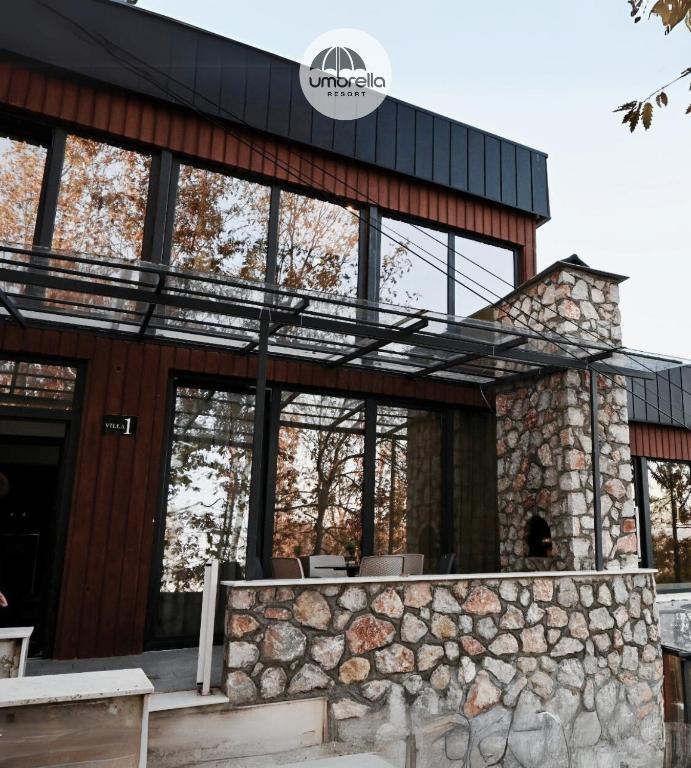 a house with a stone wall and windows at Umbrella Resort & Villas in Prishtinë