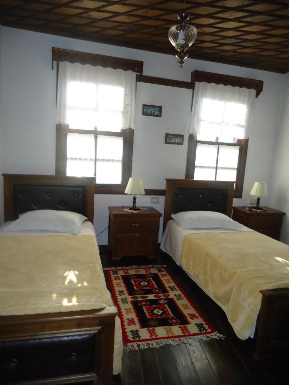 two beds in a room with two windows and a rug at Hotel Klea in Berat
