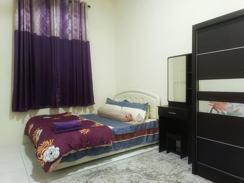 a bedroom with a bed with purple curtains and a dresser at Chek Embun Homestay in Padang Besar