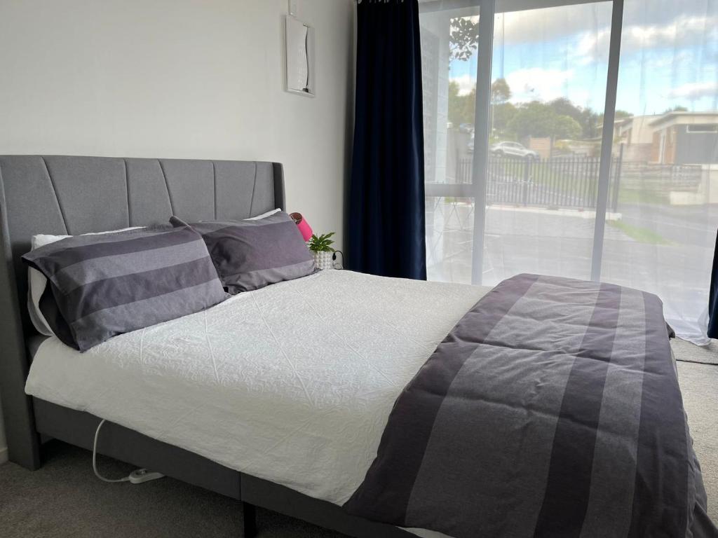 a bed in a bedroom with a large window at Totara Vale, Free Coffee, parking and wifi, near Glenfield Mall and highway 18,1 in Auckland