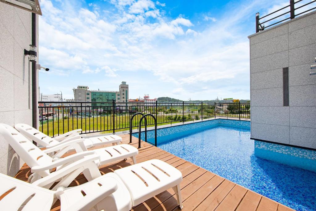 a deck with white chairs and a swimming pool at Gangneung Nishi Spa Pension in Kyŏngp'o-mal
