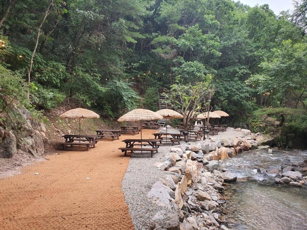 a group of picnic tables with umbrellas next to a river at Chuncheon inyeonga pension in Wikkŏndŭrae