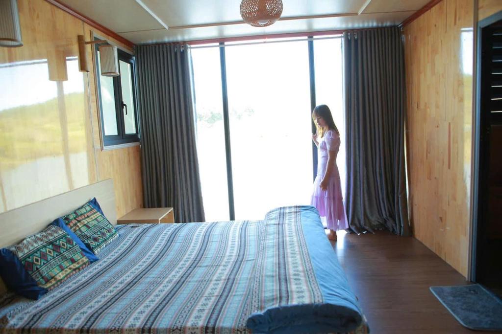Una donna in piedi in una camera da letto che guarda fuori dalla finestra di NaNa Farm a Bak Kan
