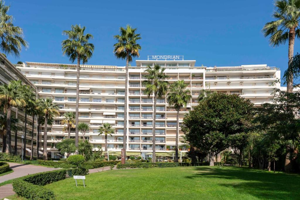 un grand bâtiment blanc avec des palmiers et un parc dans l'établissement REF 1380 - Cannes Croisette - Apartment for rent, à Cannes