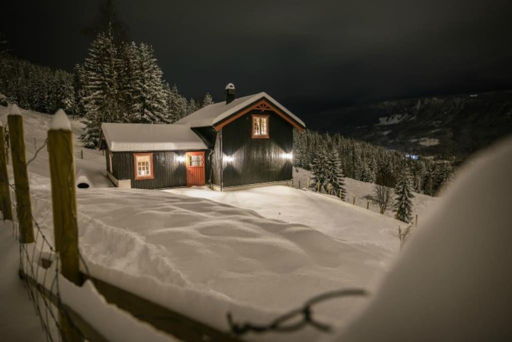 eine Hütte im Schnee mit eingeschaltetem Licht in der Unterkunft Unikt gårdshus - Gamlestua in Vestre Gausdal