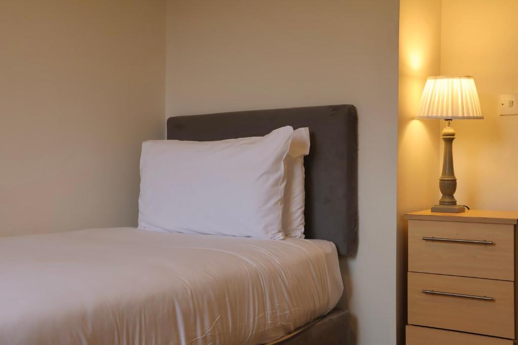 a bed with a white pillow and a lamp on a dresser at Doolin Village Lodges in Doolin