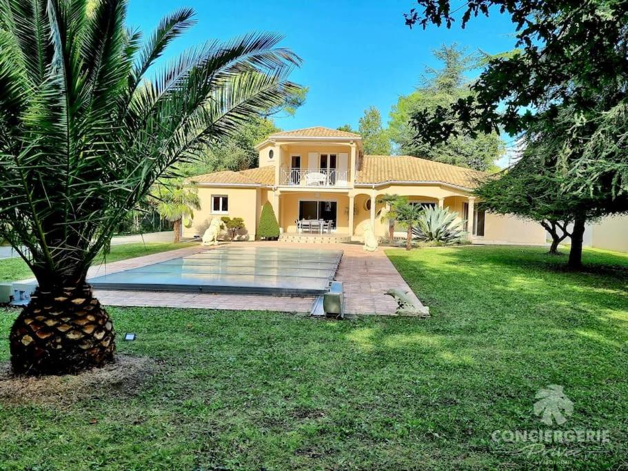 une grande maison avec un palmier dans la cour dans l'établissement Spacieuse et confortable villa avec piscine - L'Impériale, à La Tremblade