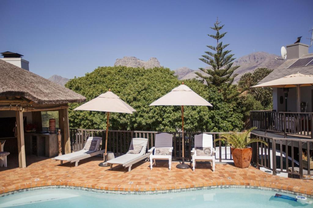 a swimming pool with two chairs and umbrellas at Chapman's Peak Bed and Breakfast in Hout Bay