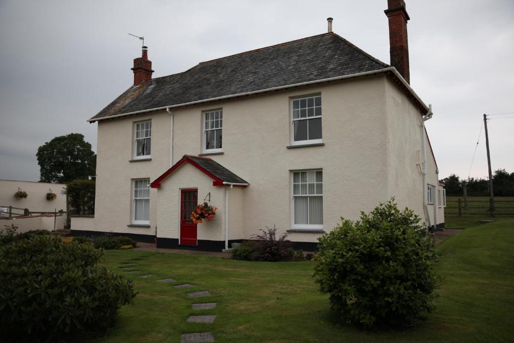 uma grande casa branca com uma porta vermelha em Weir Mill Farm em Cullompton