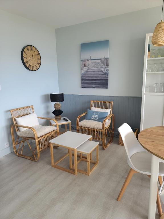 - un salon doté d'un mobilier en rotin, d'une table et d'une horloge dans l'établissement Le Front de Mer, à Saint-Jean-de-Monts