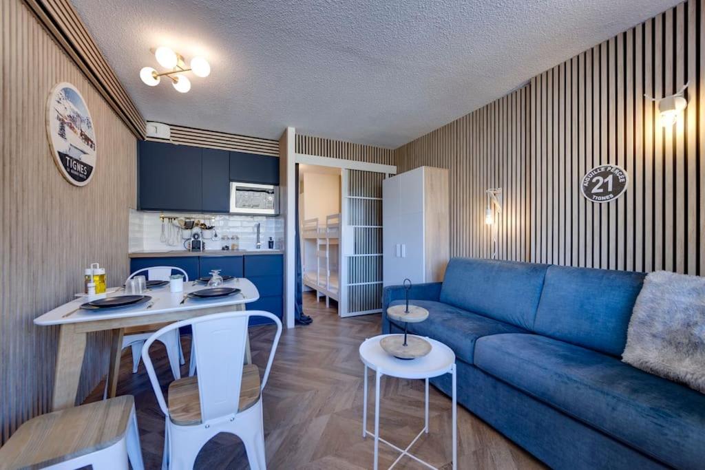 Una sala de estar con un sofá azul y una cocina. en Au 6ème ciel Tignes 2100m - Vue Lac & Montagnes - Proche pistes - 2 adultes et 2 enfants, en Tignes