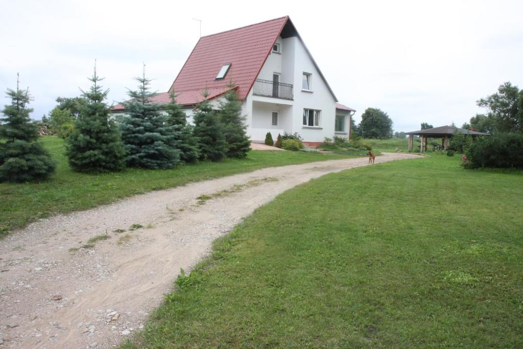 eine unbefestigte Straße, die zu einem weißen Haus mit rotem Dach führt in der Unterkunft Kempings "Ceļmalnieki" in Liepāja