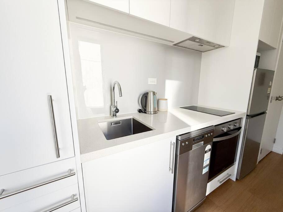 a small white kitchen with a sink and a refrigerator at Hot Deal! Sky Stars Central Haven Studio with nice pool In CBD heart in Auckland