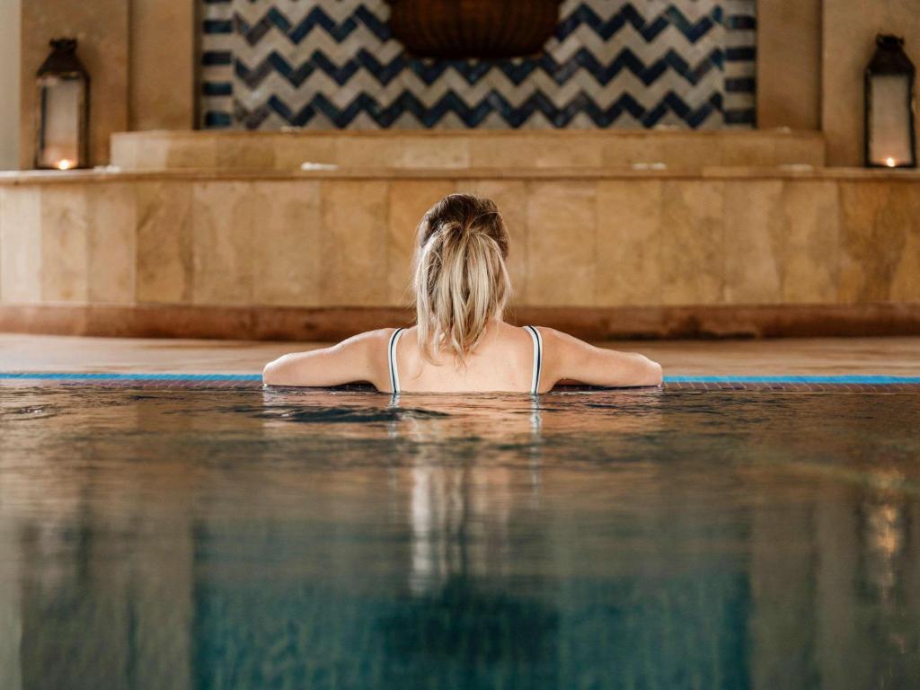 a woman is sitting in a swimming pool at Le Médina Essaouira Thalassa Sea & Spa - MGallery Collection in Essaouira