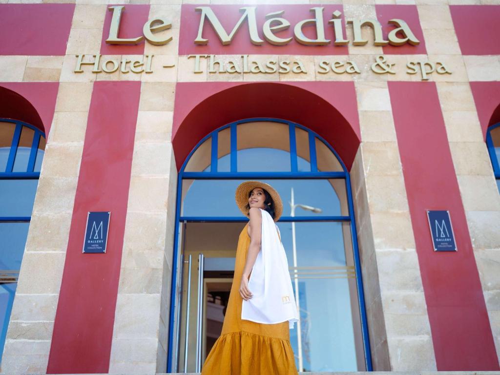 a woman in a hat standing in front of a building at Le Médina Essaouira Thalassa Sea & Spa - MGallery Collection in Essaouira