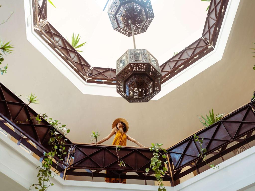 a woman standing on a balcony with a chandelier at Le Médina Essaouira Thalassa Sea & Spa - MGallery Collection in Essaouira
