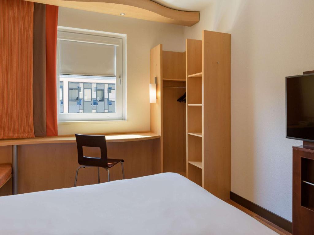 a room with a bed and a chair and a window at ibis Stuttgart Airport Messe in Leinfelden-Echterdingen