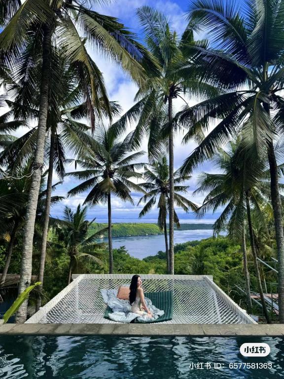 a woman sitting in a hammock in a pool with palm trees at SPICE TRADER in Nusa Penida