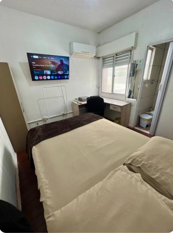 a room with two beds and a desk and a tv at Pousada DL in Pelotas