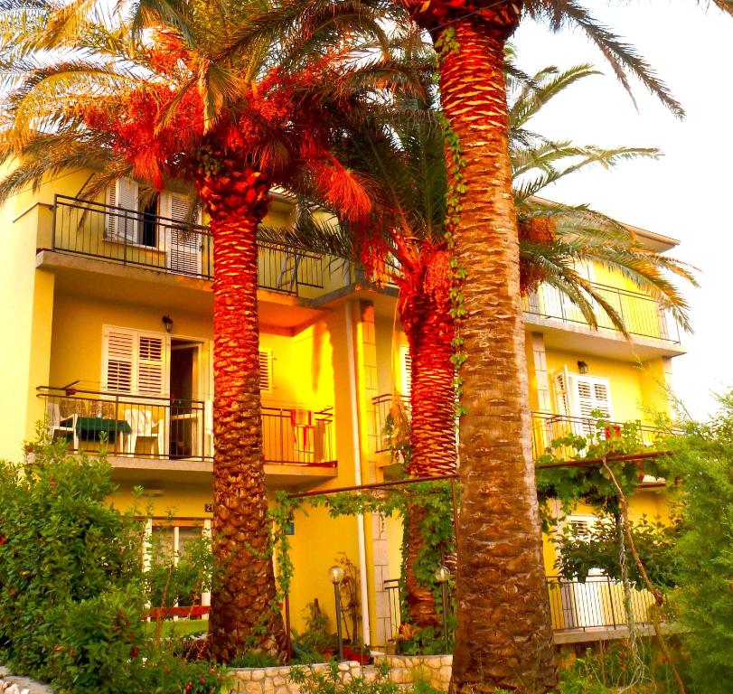 two palm trees in front of a yellow building at House Rozi in Rab