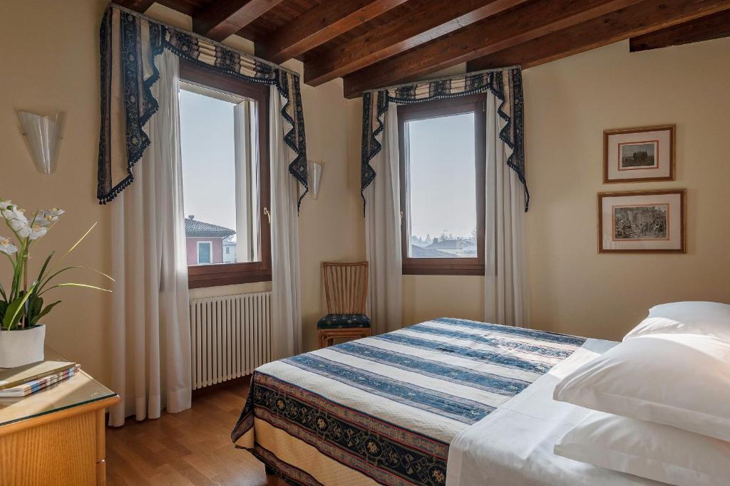 a bedroom with two windows and a bed with white sheets at Palazzo Brando - Living Apartments in Treviso