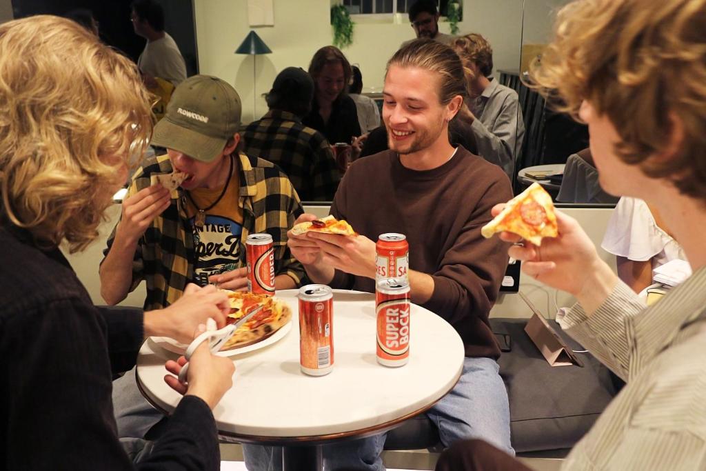 a group of people sitting around a table eating pizza at Gspot Hostels & Love Triangles Pizzeria in Lisbon